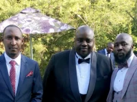 Wicknell Chivayo berfoto bersama dua pria berjas di taman resepsi di Harare