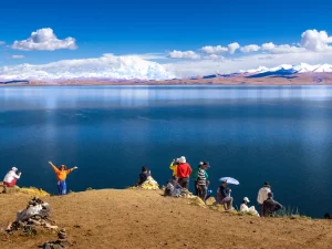 Ilustrasi rombongan wisatawan di tepi bukit menghadap Danau Namtso dan pegunungan bersalju, Tibet, Tiongkok