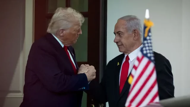 Donald Trump dan Benjamin Netanyahu berjabat tangan di Gedung Putih dengan bendera Amerika Serikat dan Israel di latar belakang